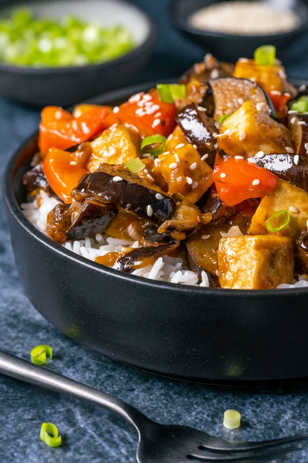 Eggplant tofu stir fry with rice in a black bowl.