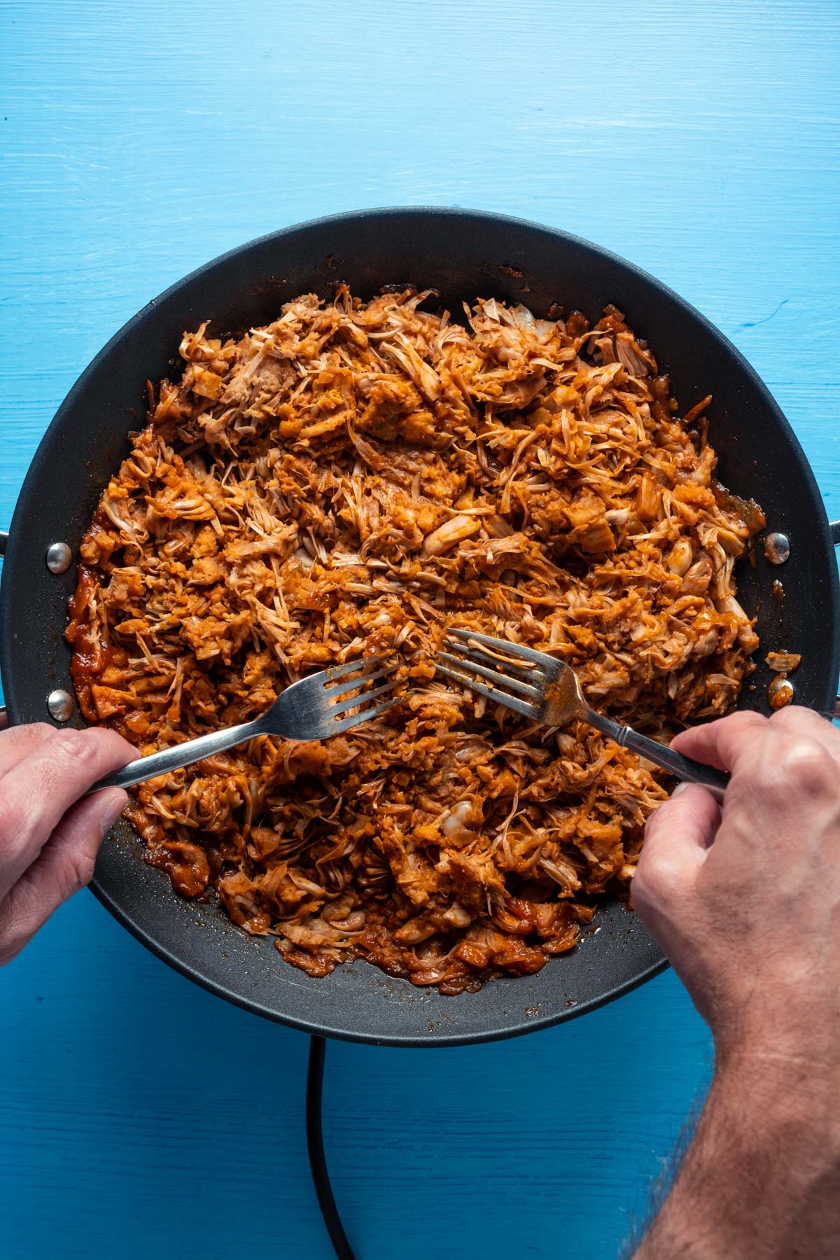 Two forks shredding cooked jackfruit in a frying pan.