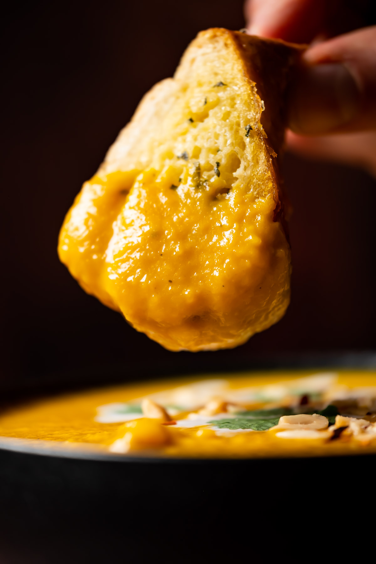 Garlic bread dipping into a bowl of Thai butternut squash soup.