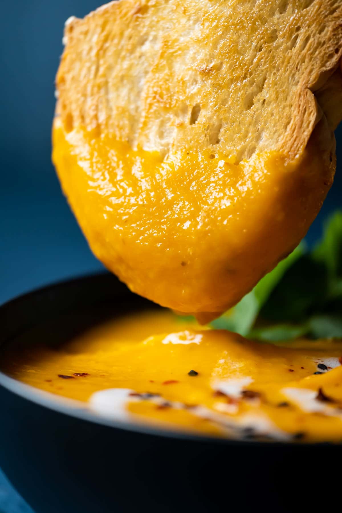 Slice of toasted bread dipping into a bowl of Thai sweet potato soup.