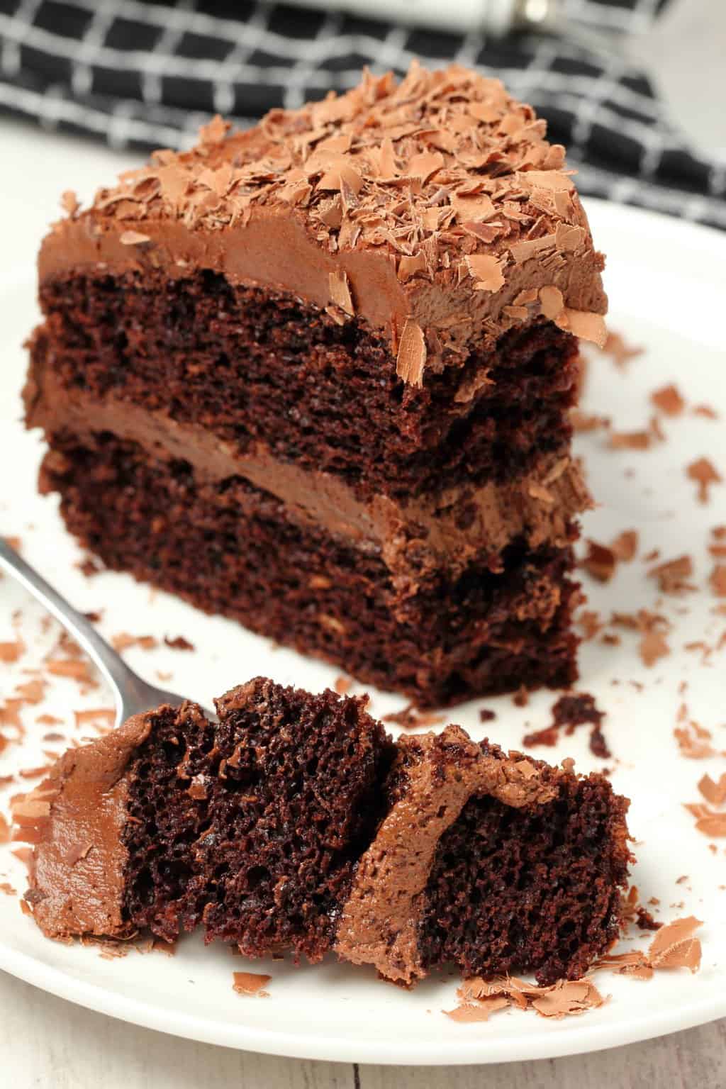 A slice of vegan chocolate cake on a white plate with a cake fork.