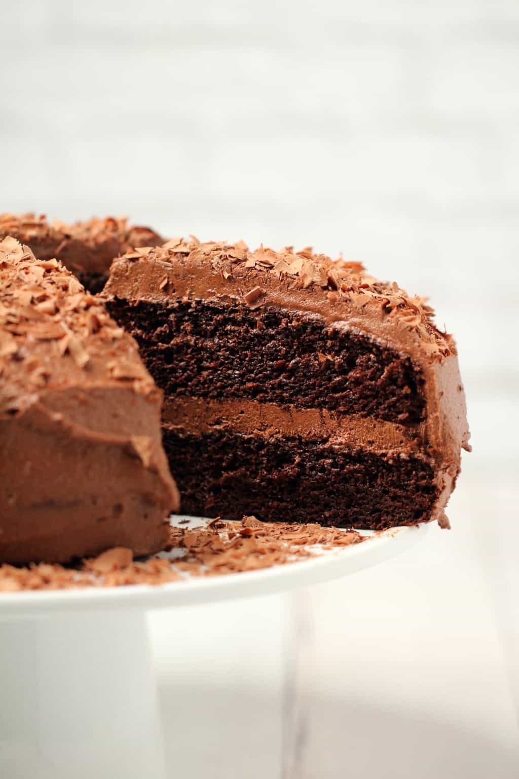 Chocolate cake with one slice cut and ready to serve on a white cake stand. 