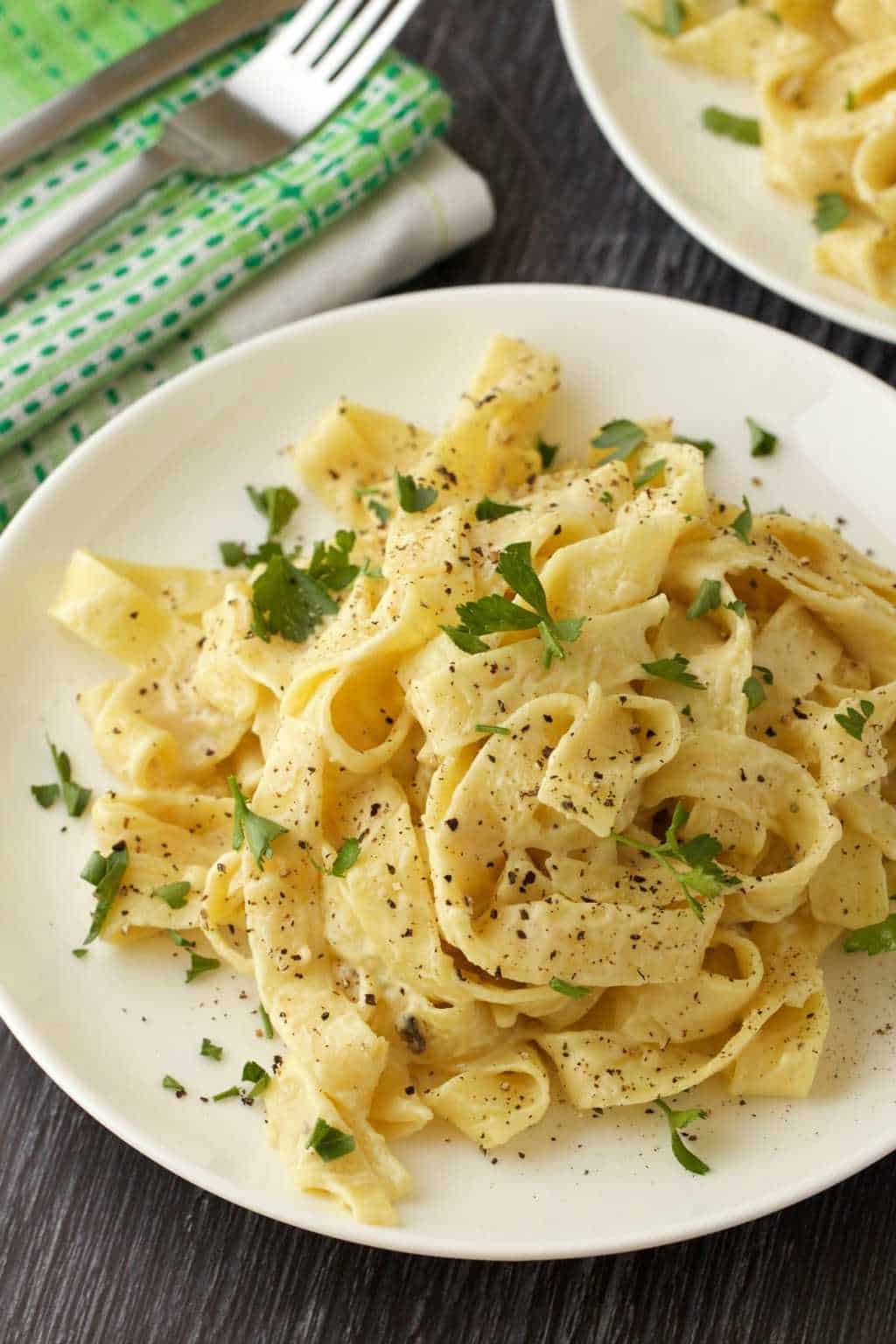 Vegan fettucine with alfredo sauce and fresh parsley on a white plate. 