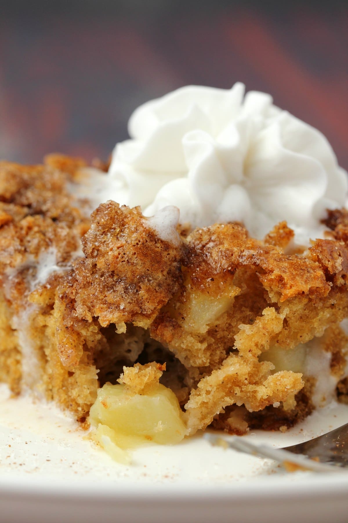 Slice of vegan apple cake topped with vegan whipped cream on a white plate. 