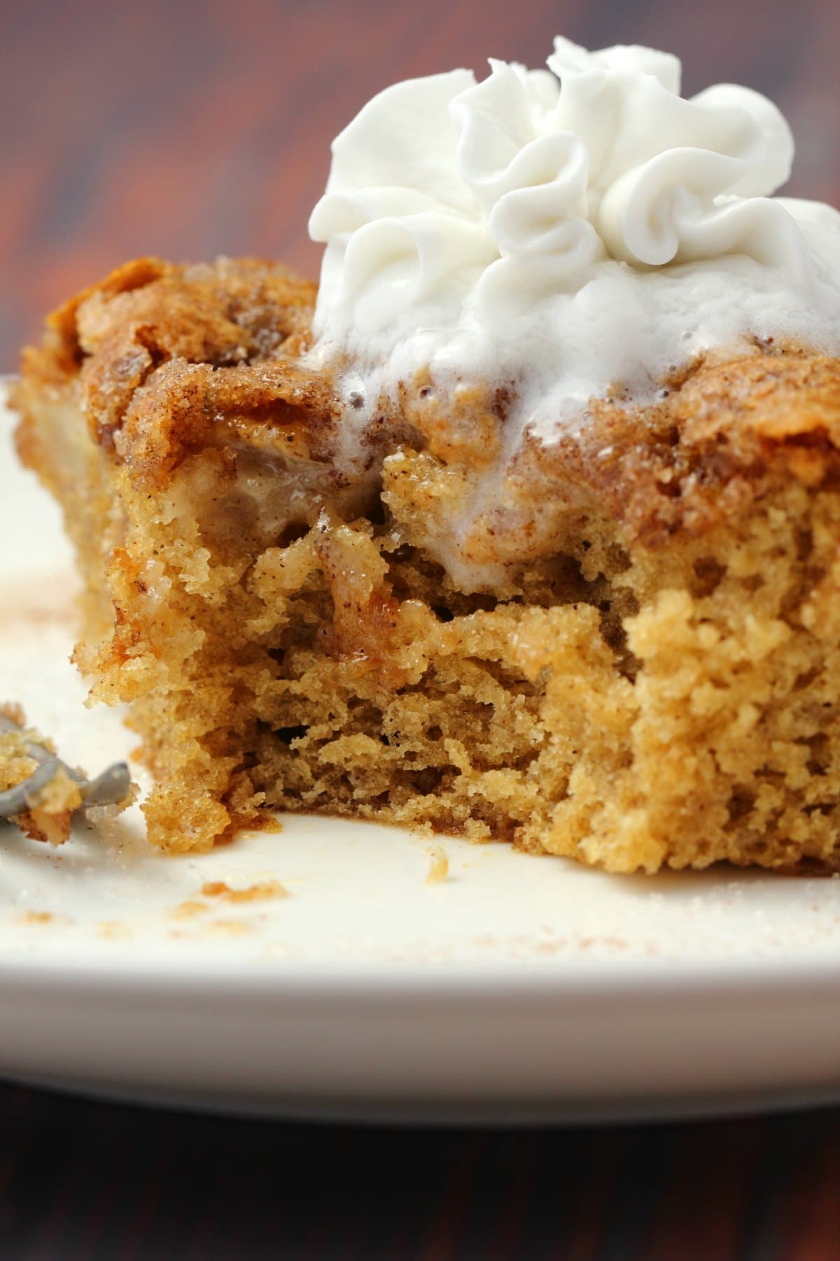 Slice of vegan apple cake topped with vegan whipped cream on a white plate with a cake fork. 