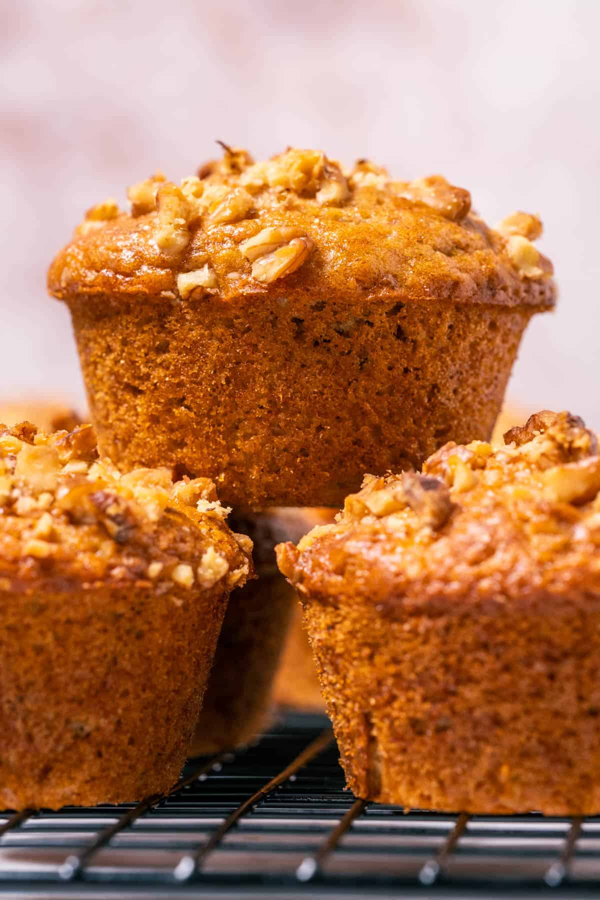 Vegan banana bread muffins stacked up on a wire cooling rack.