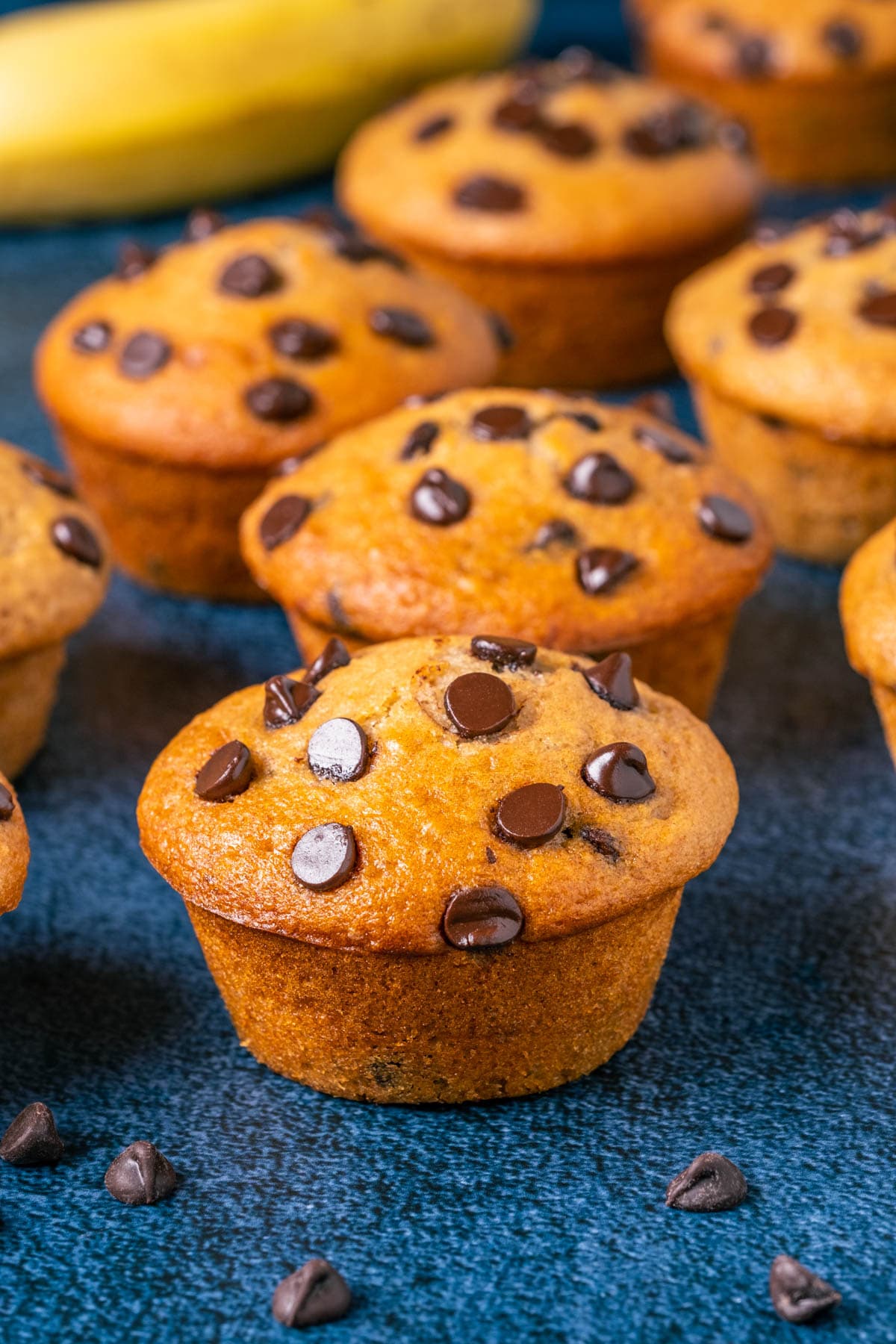 Vegan banana chocolate chip muffins with banana in the background.