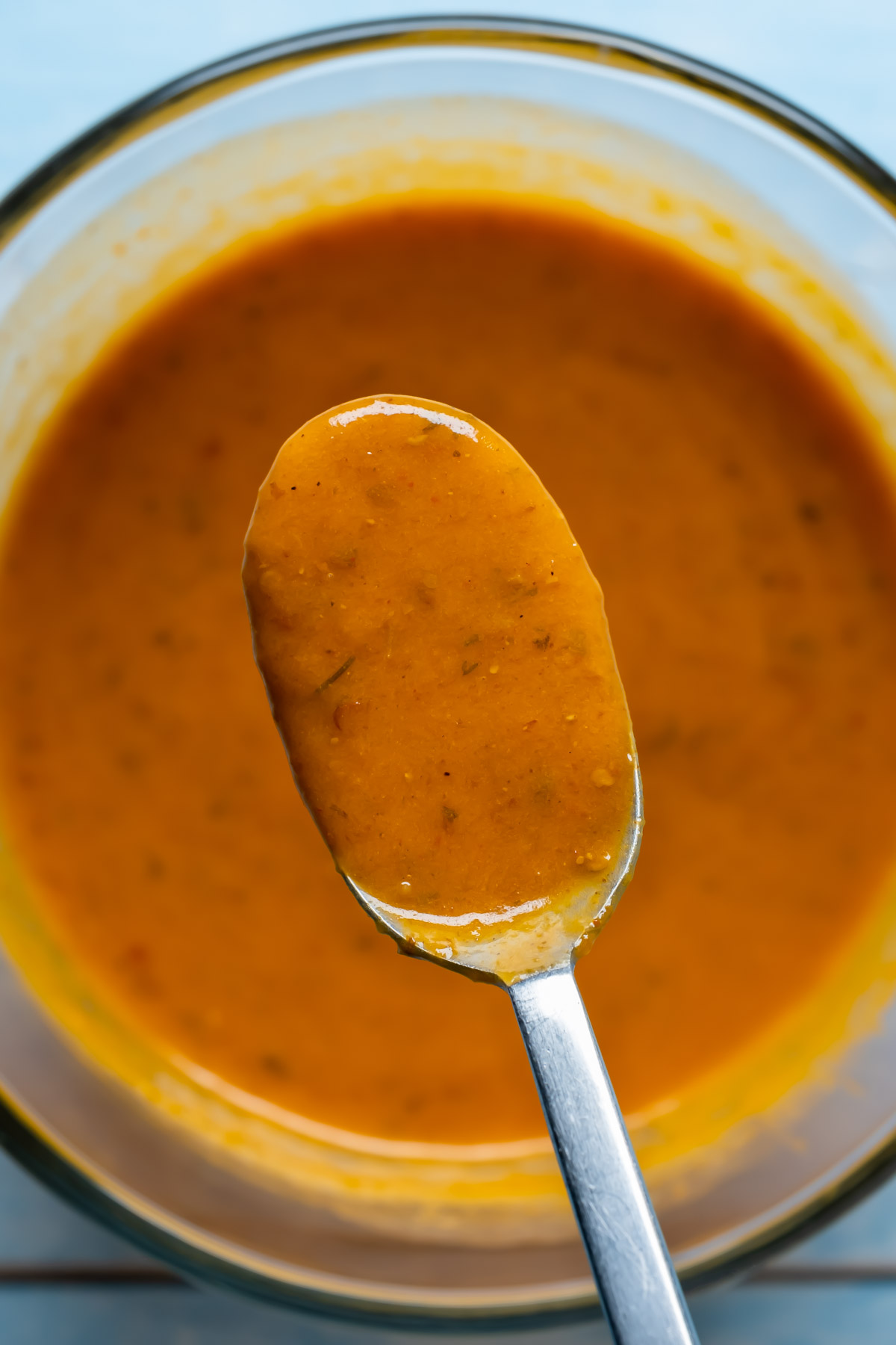 Vegan buffalo sauce in a glass bowl with a spoon.