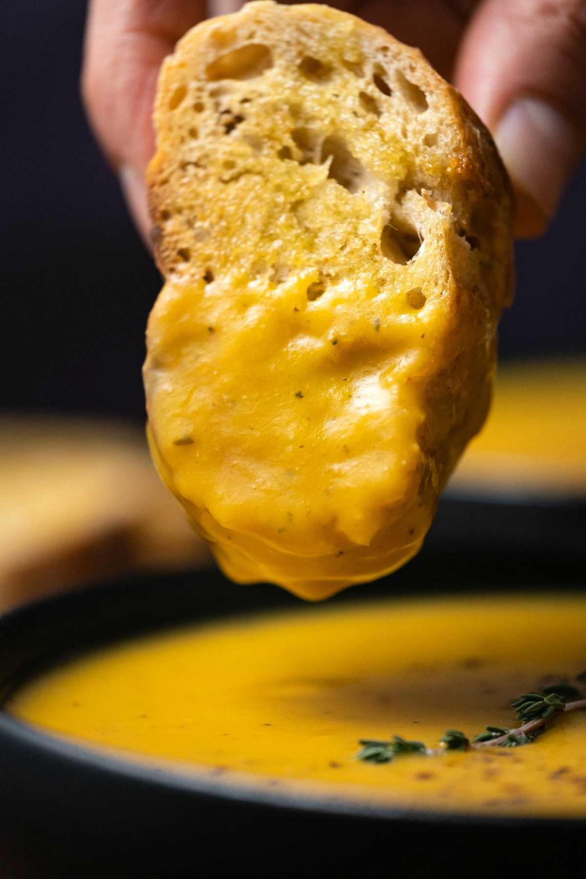 Slice of bread dipping into a bowl of butternut squash soup.