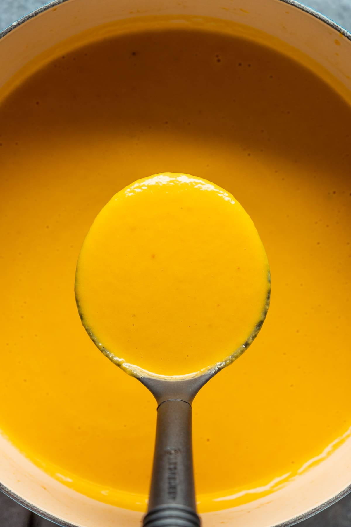 Blended carrot soup in a pot with a soup ladle.