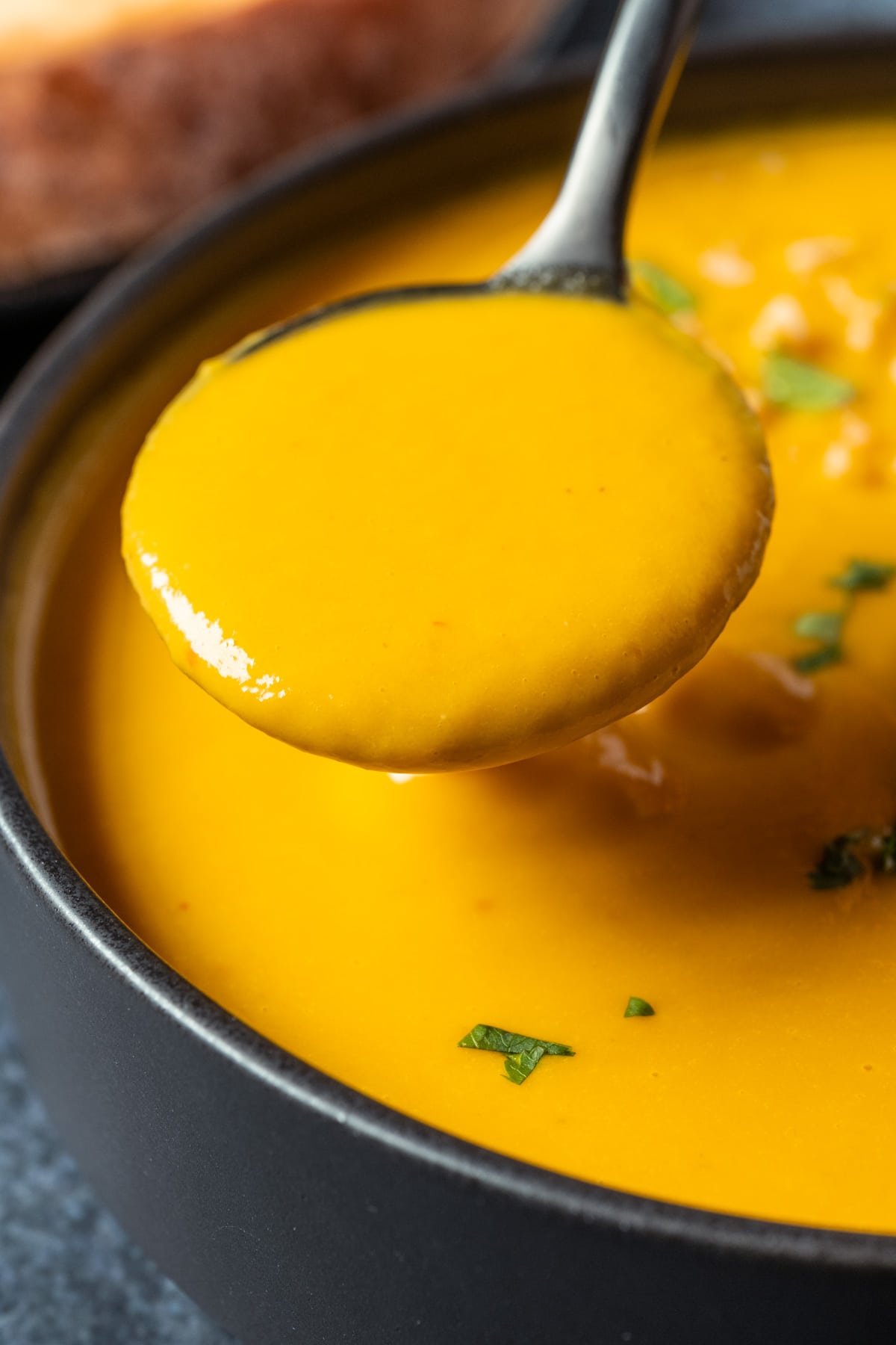 Vegan carrot soup in a black bowl with a spoon.