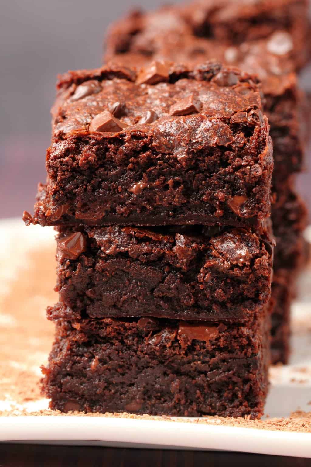 Vegan chocolate brownies stacked up on a white plate. 