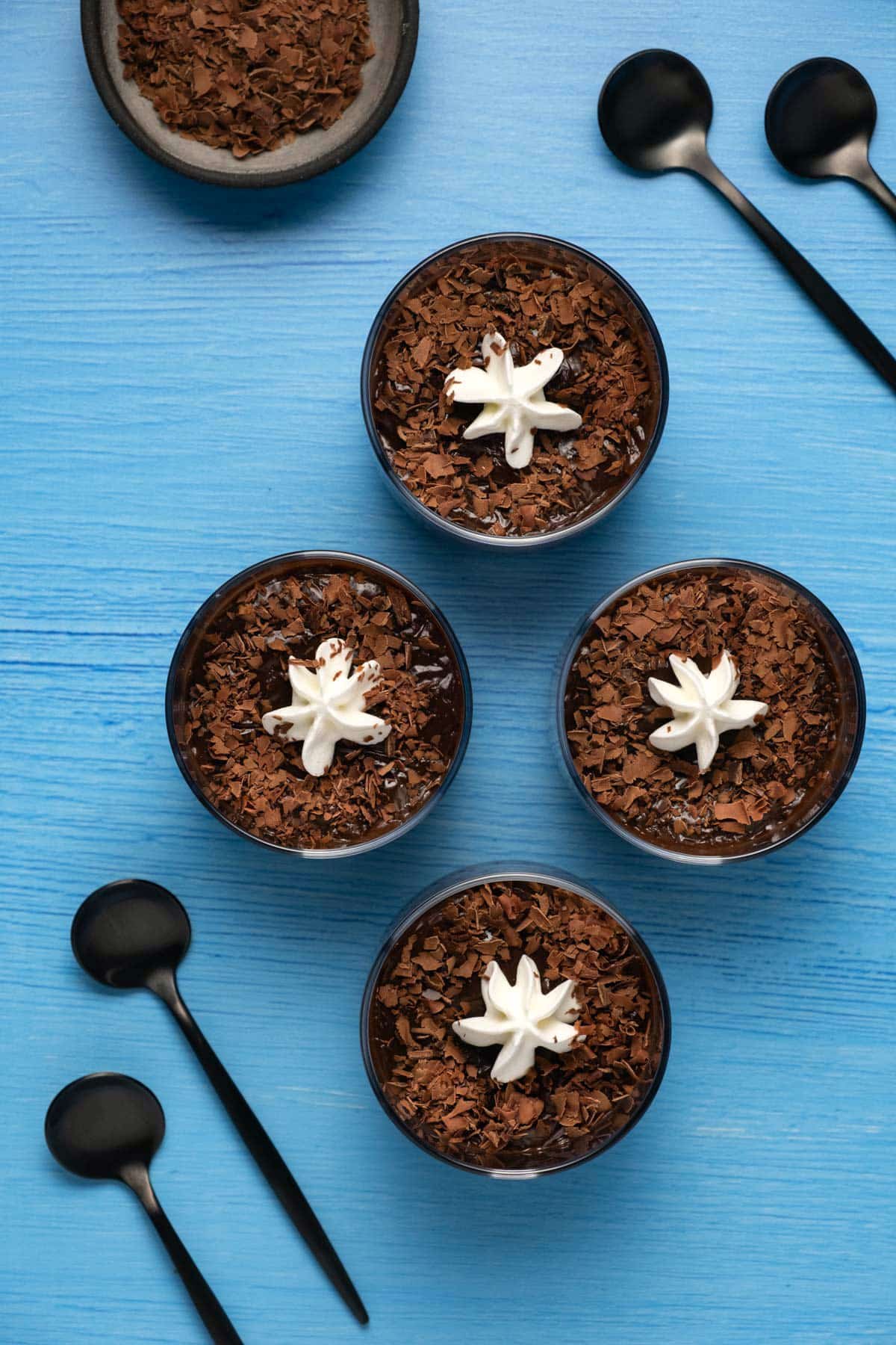 Vegan chocolate pudding in ramekins topped with chocolate shavings and vegan whipped cream.