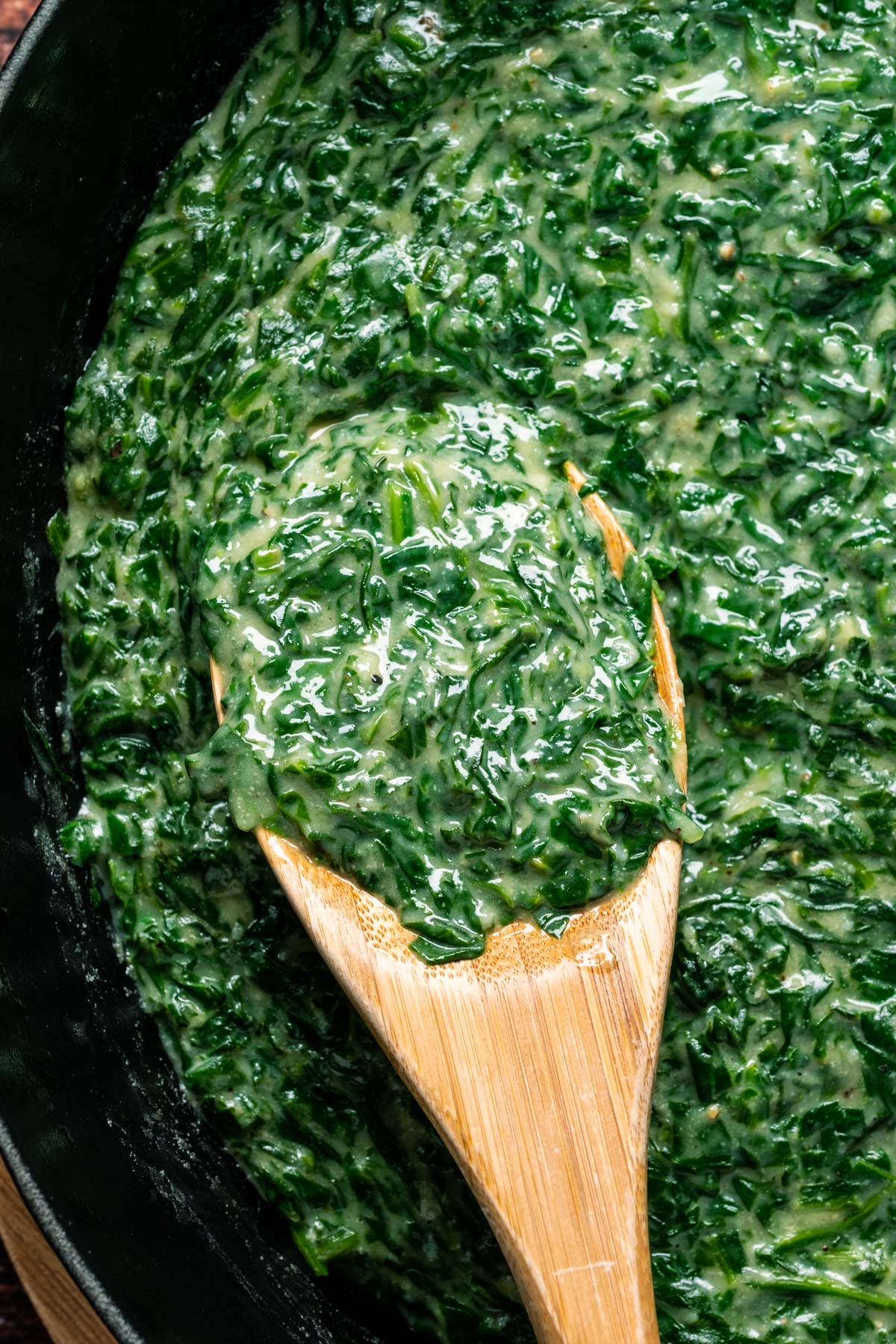 Vegan creamed spinach in a skillet with a wooden spoon.