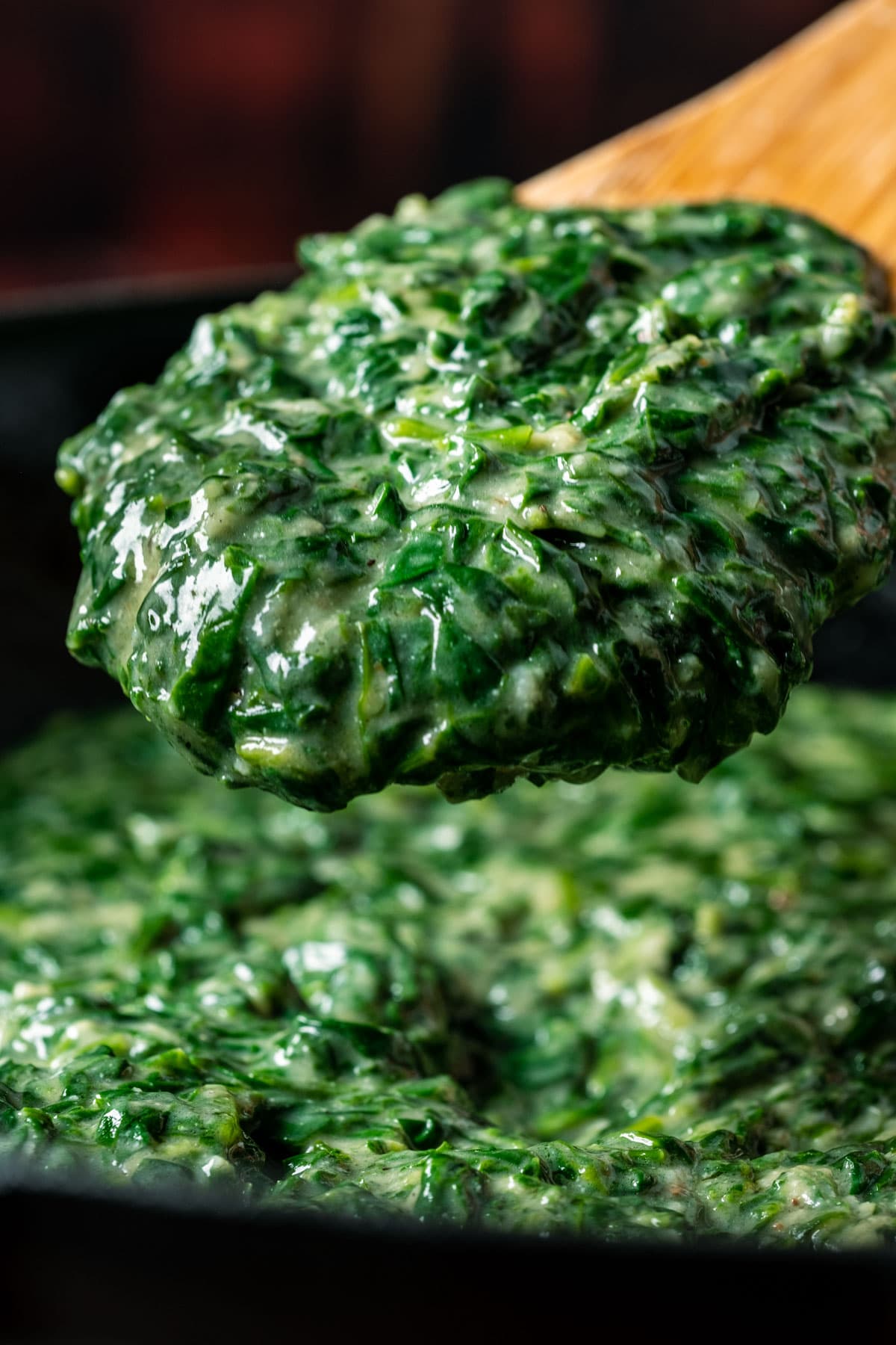 Vegan creamed spinach in a skillet with a wooden spoon.