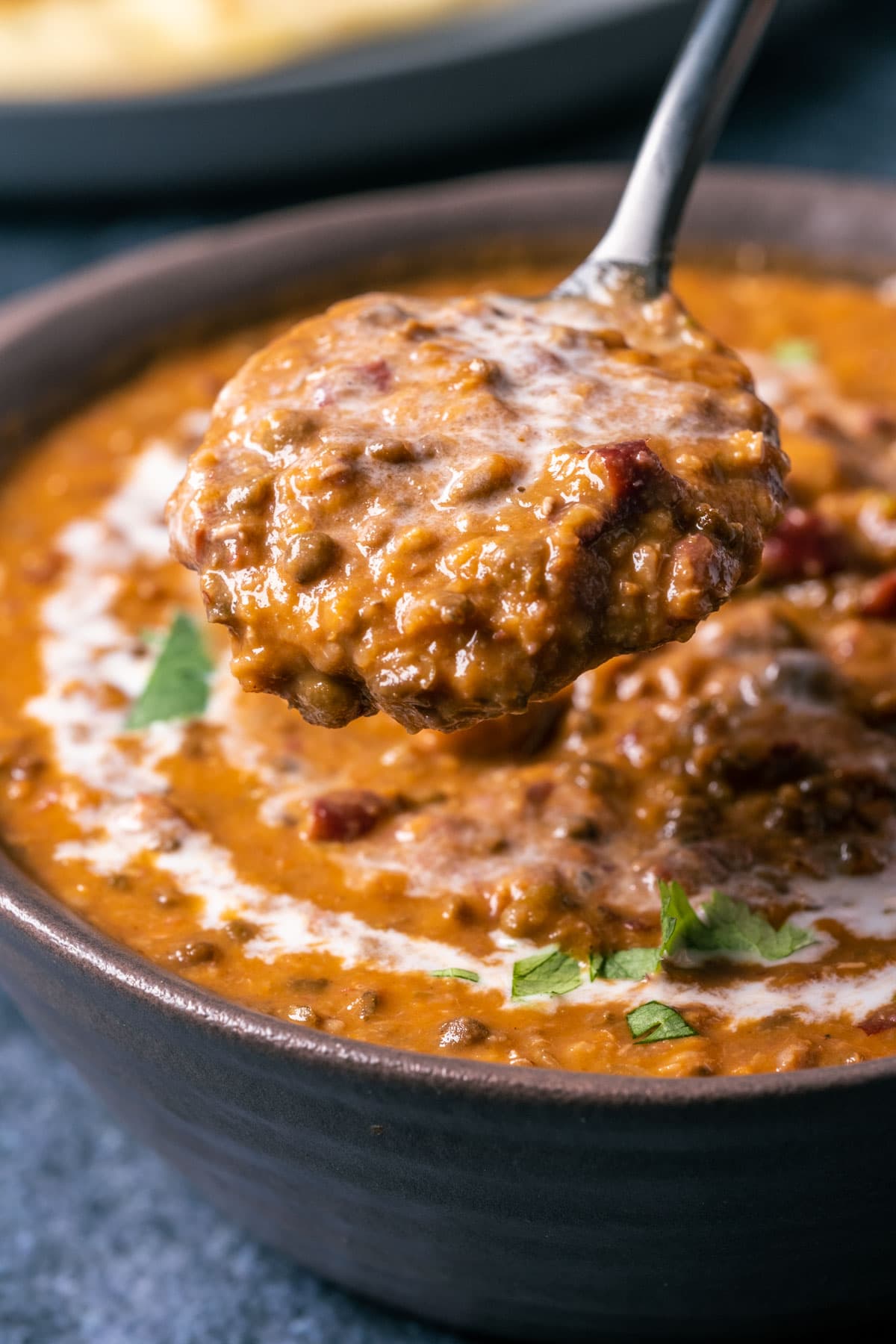 Vegan dal makhani topped with a drizzle of coconut cream and fresh chopped cilantro in a brown bowl with a spoon.