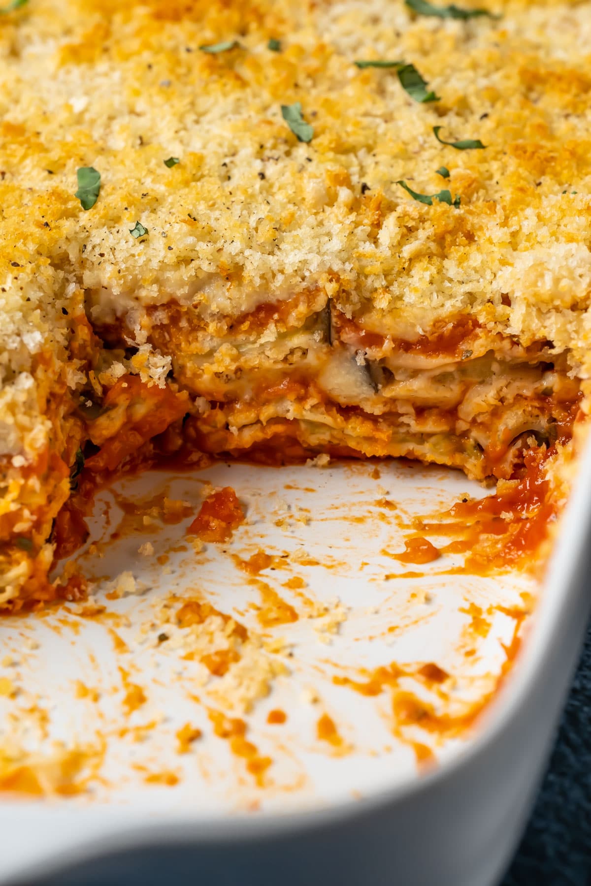 Vegan eggplant parmesan in a white dish with slices removed.