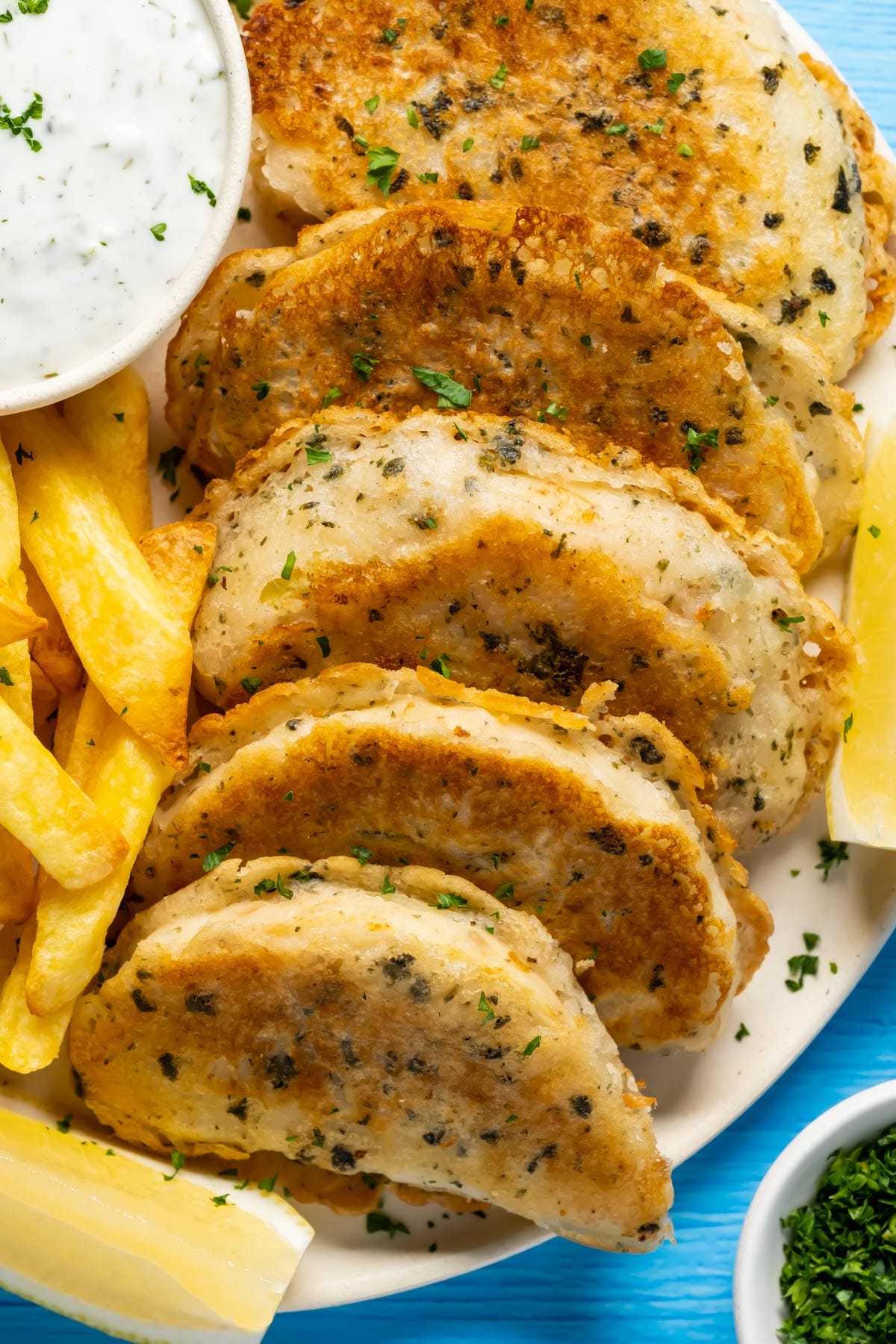 Beer battered vegan fish with chips, vegan tartar sauce and fresh lemon on a plate.