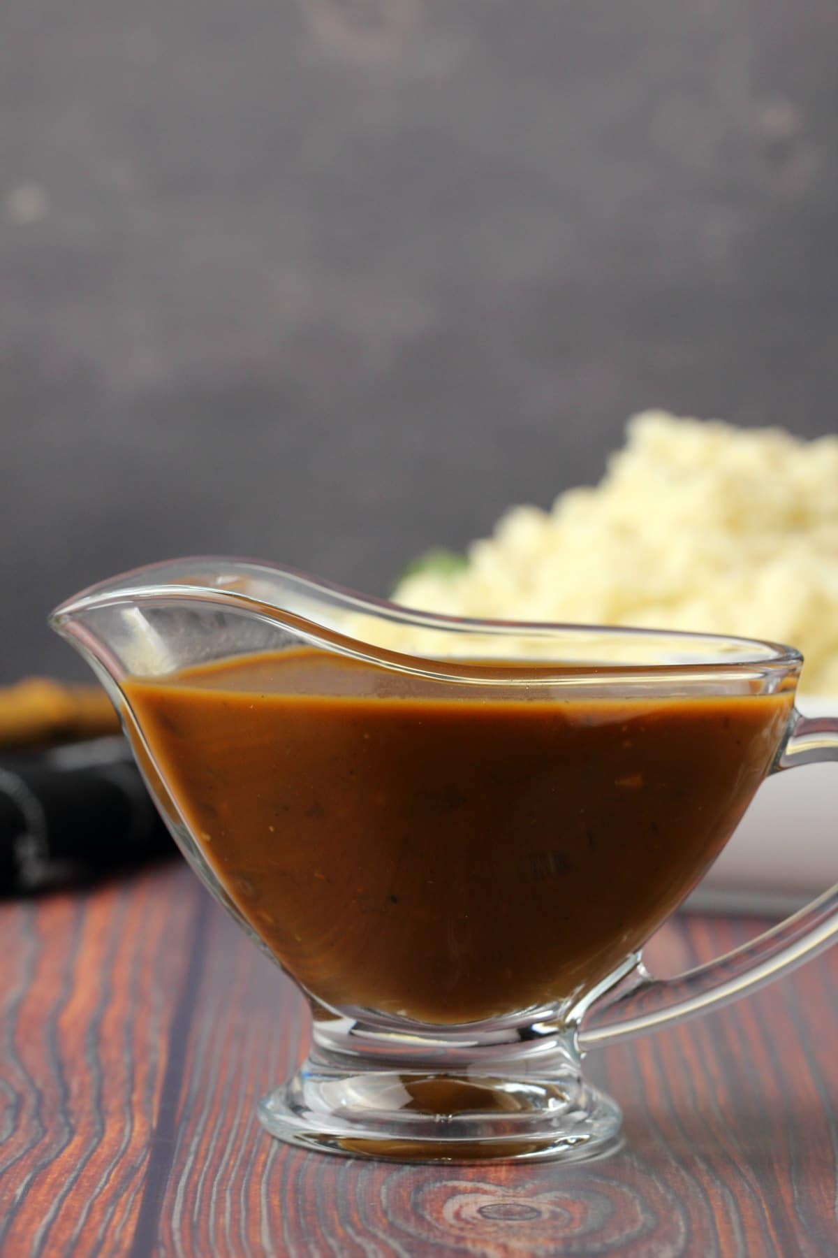 Gravy in a glass gravy jug with mashed potatoes in the background. 