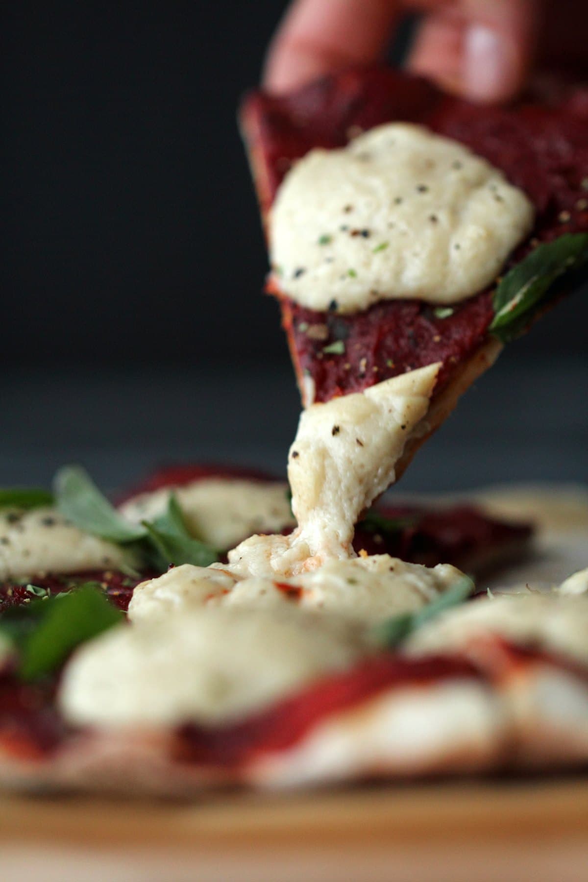 A slice of pizza with melted vegan mozzarella on is lifted up. 