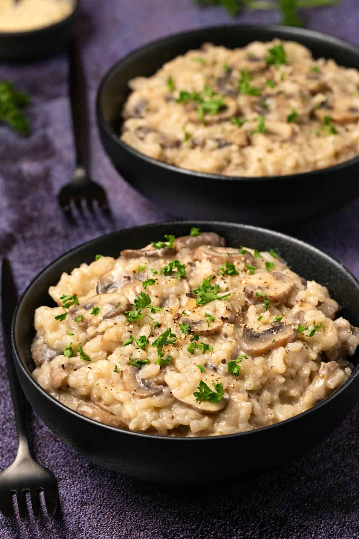 Vegan mushroom risotto in a black bowl with fresh parsley. 