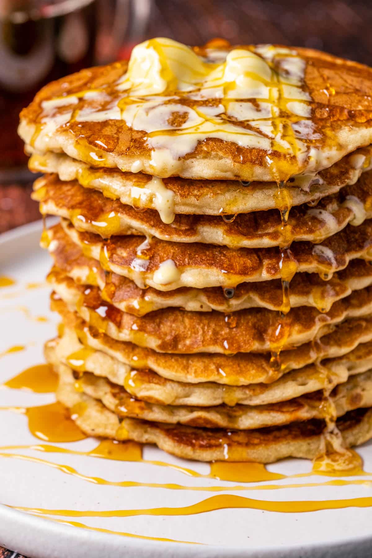 Stack of vegan oatmeal pancakes topped with vegan butter and syrup on a white plate.