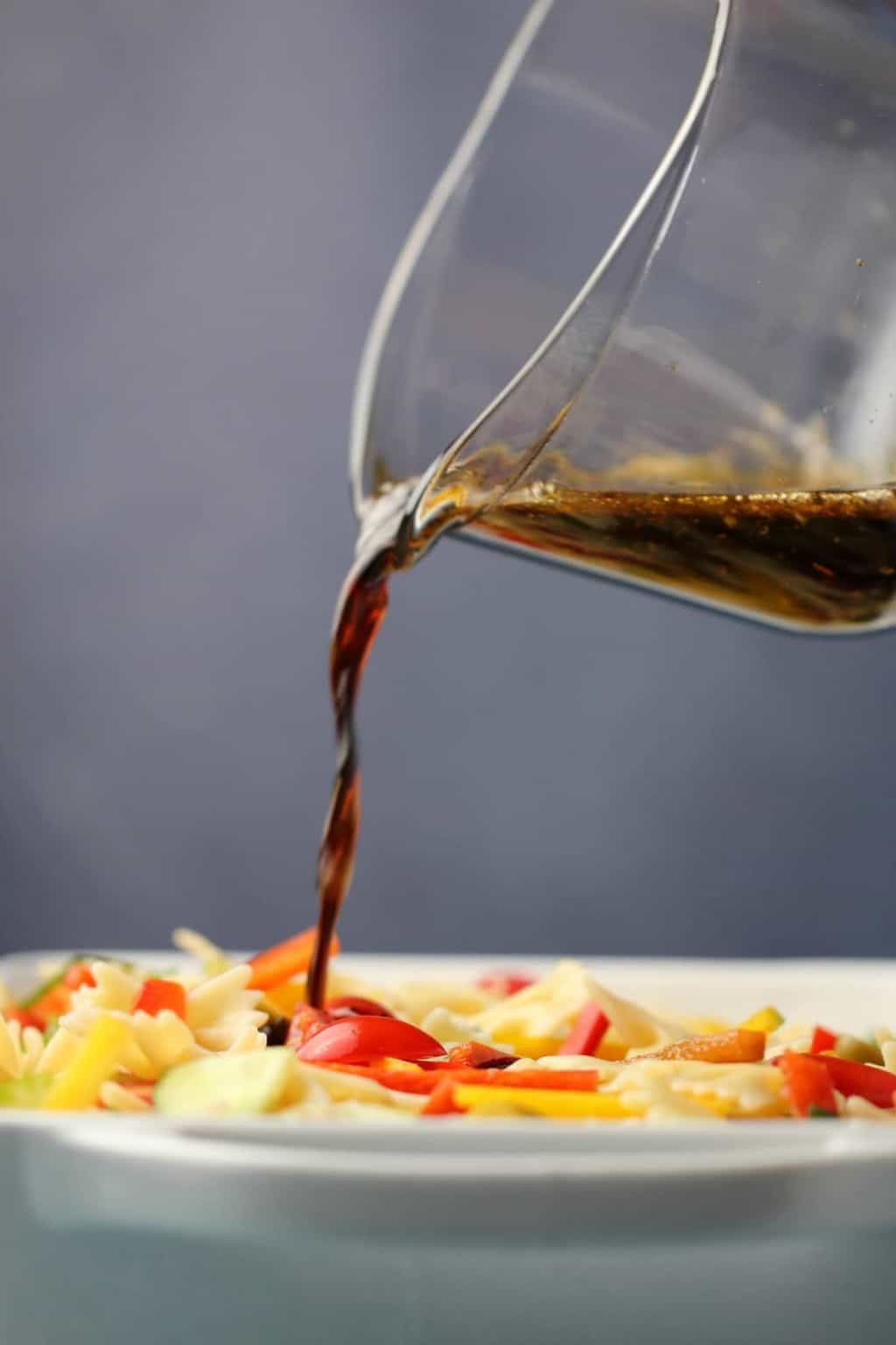 Pouring sesame dressing over a vegan pasta salad. 