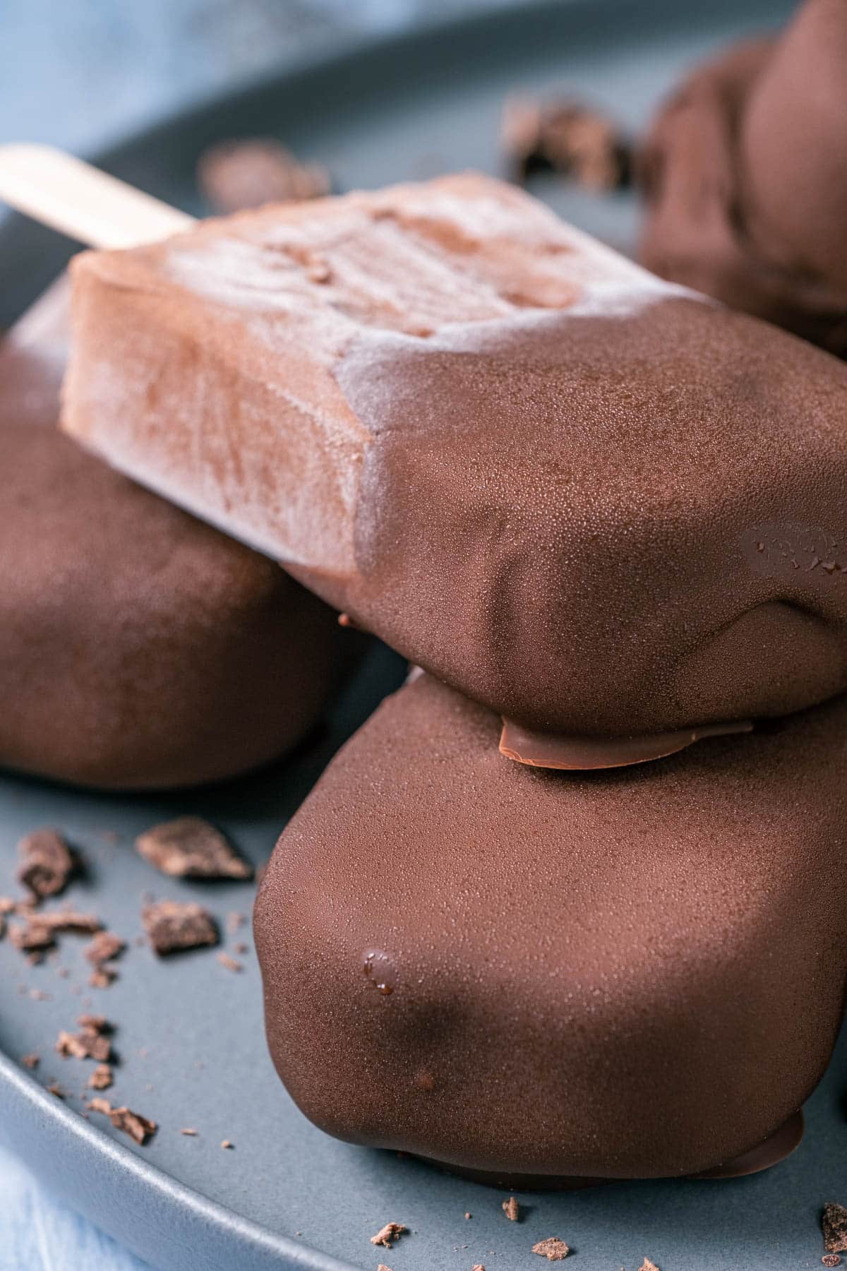 Chocolate dipped popsicles stacked up on a plate.