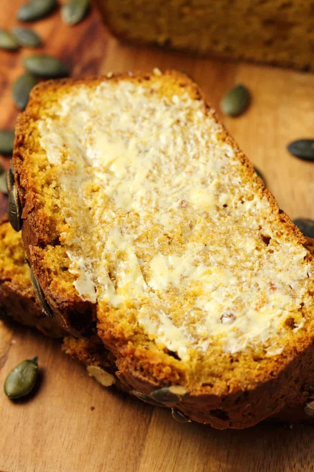 Slices of buttered vegan pumpkin bread on a wooden board. 