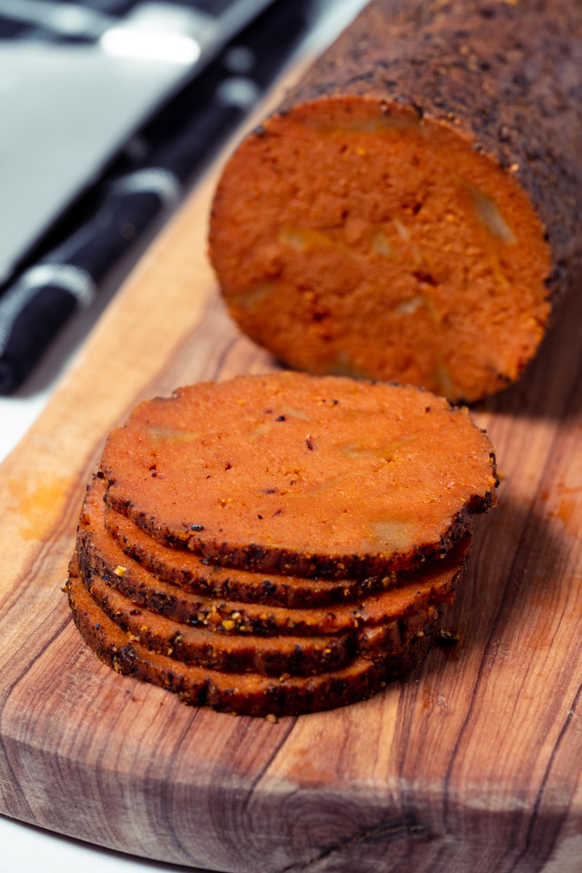 Slices of vegan salami stacked up on a wooden board.