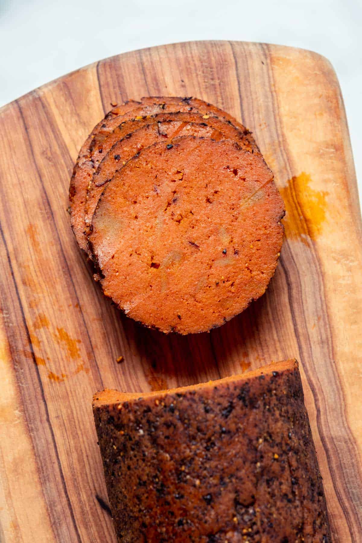 Slices of vegan salami stacked up on a wooden board.