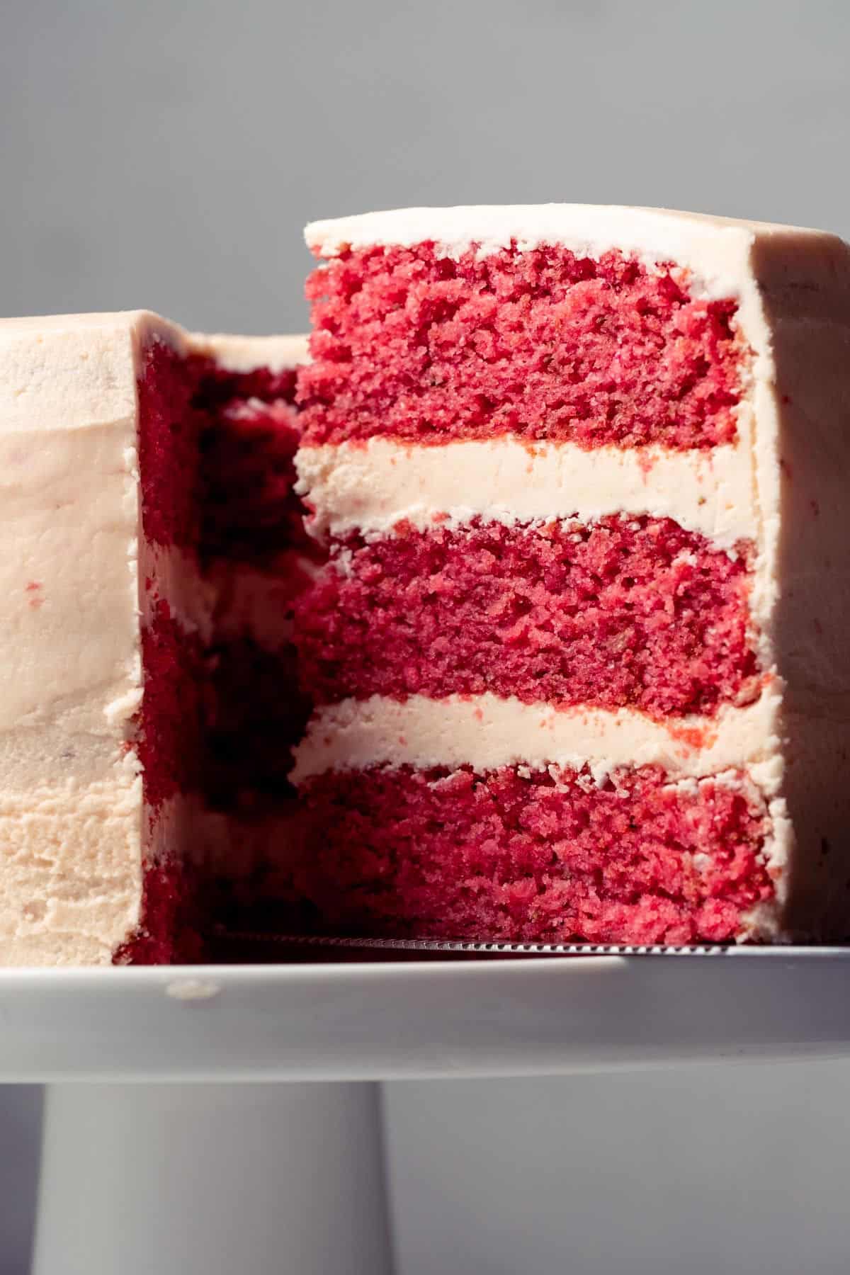 Strawberry cake on a white cake stand with one slice cut and ready to serve.