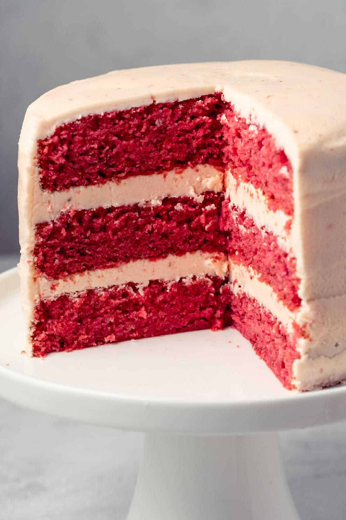 Strawberry cake with slices removed on a white cake stand.