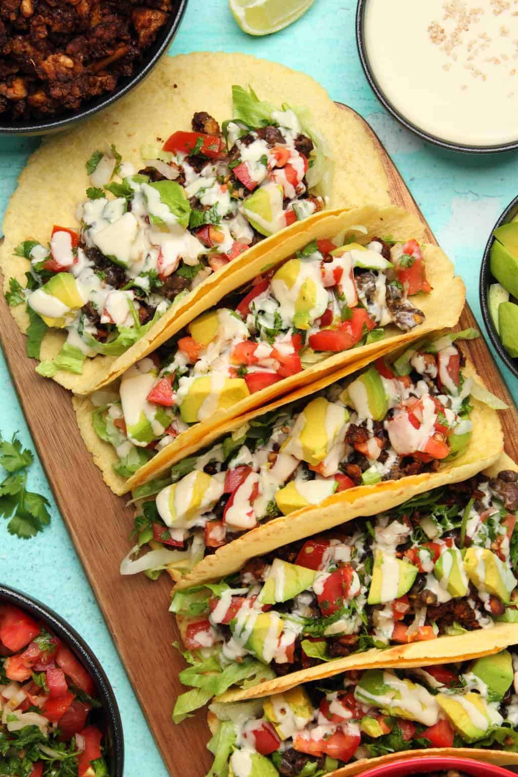 Vegan tacos lined side by side up on a wooden board. 