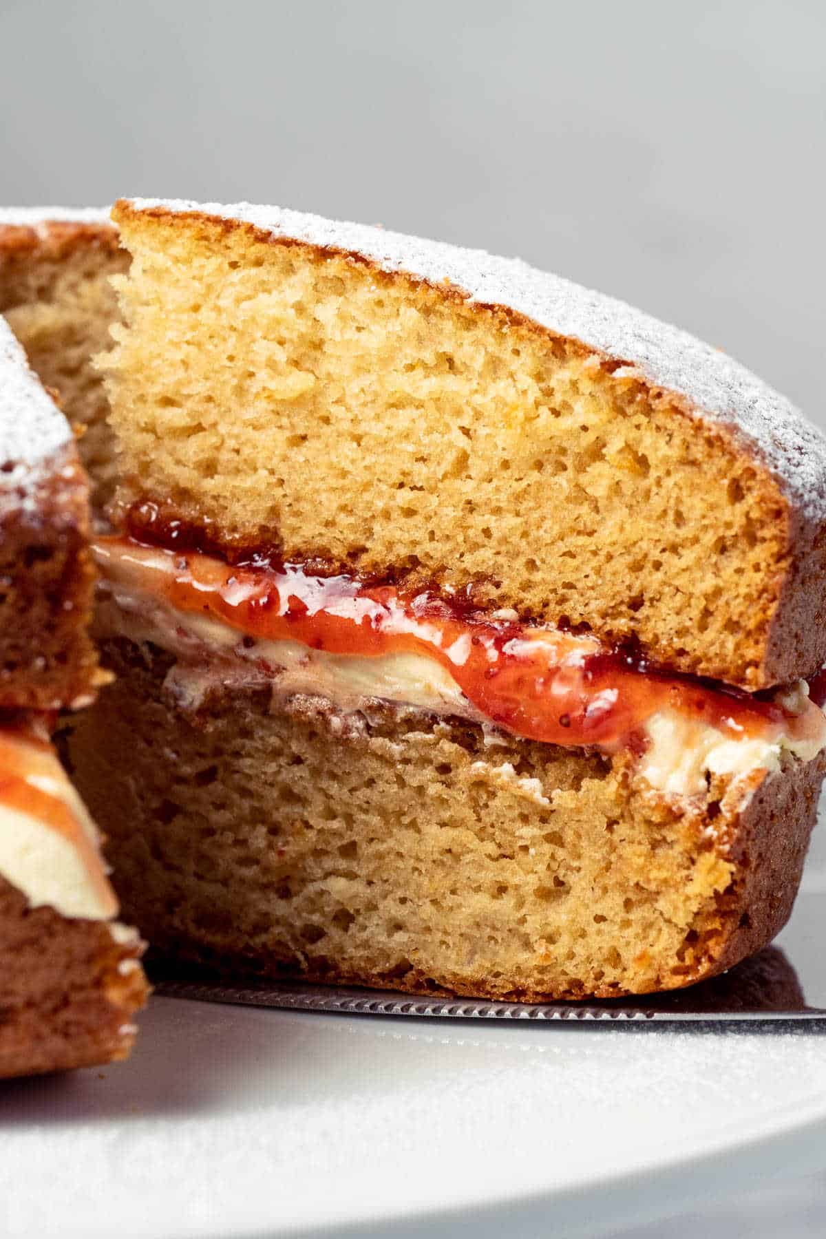 Vegan Victoria sponge with one slice cut on a white cake stand.