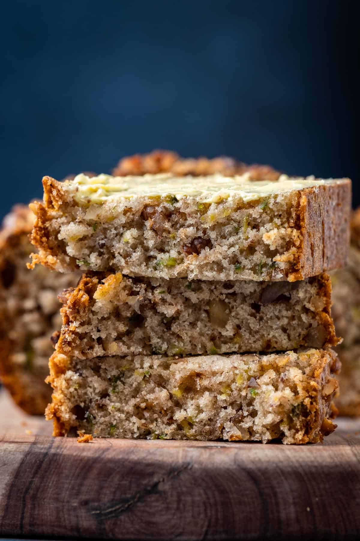 Slices of buttered vegan zucchini bread stacked up on a wooden board.